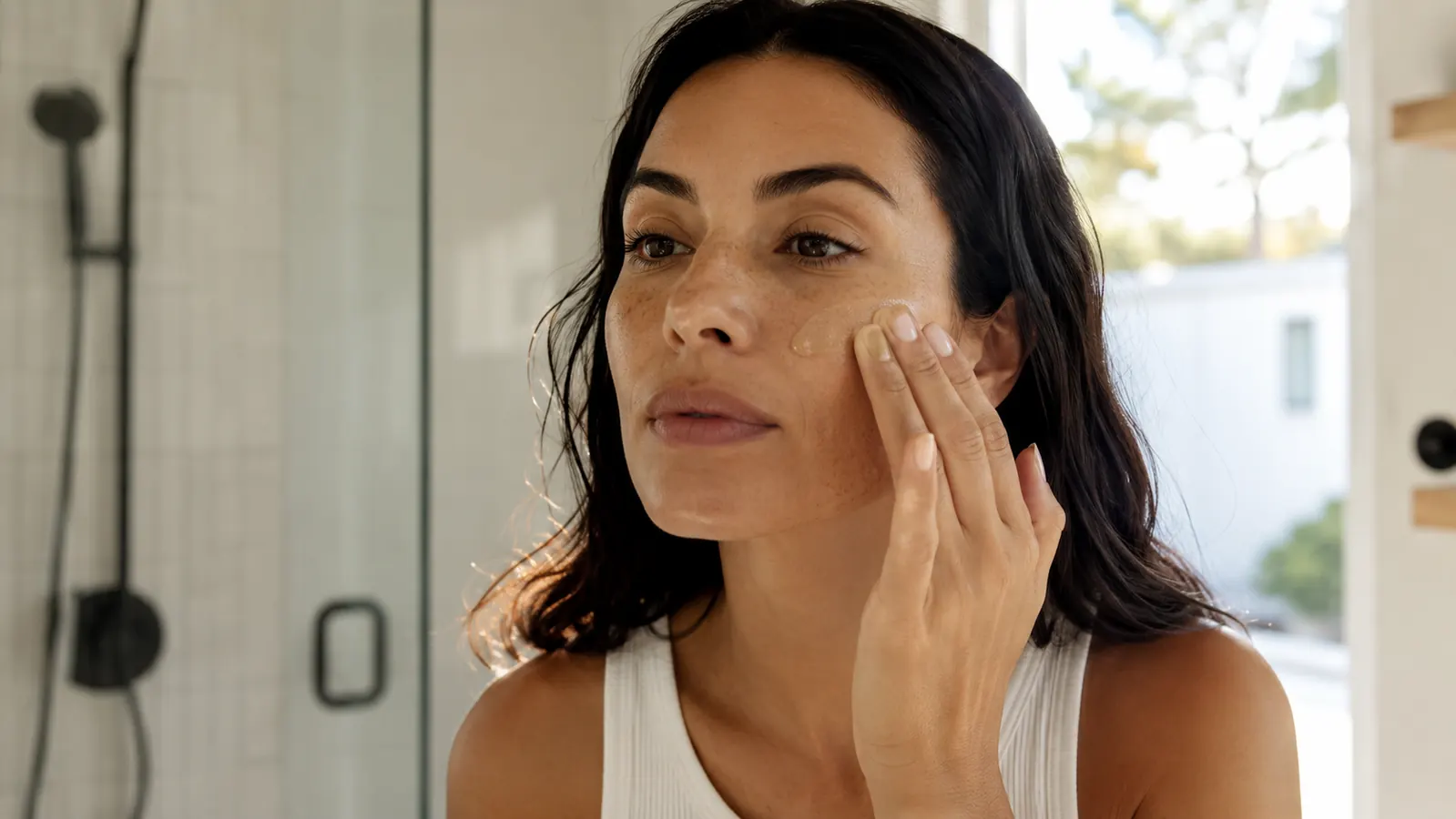 Woman pressing mineral sunscreen into skin in soft morning bathroom light