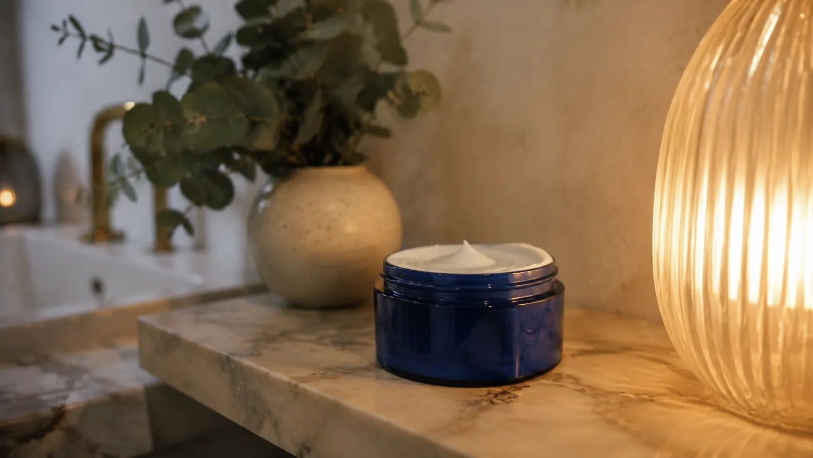 A jar of CeraVe Skin Renewing Night Cream on a marble bathroom shelf next to a small plant, soft warm bedside lamp light