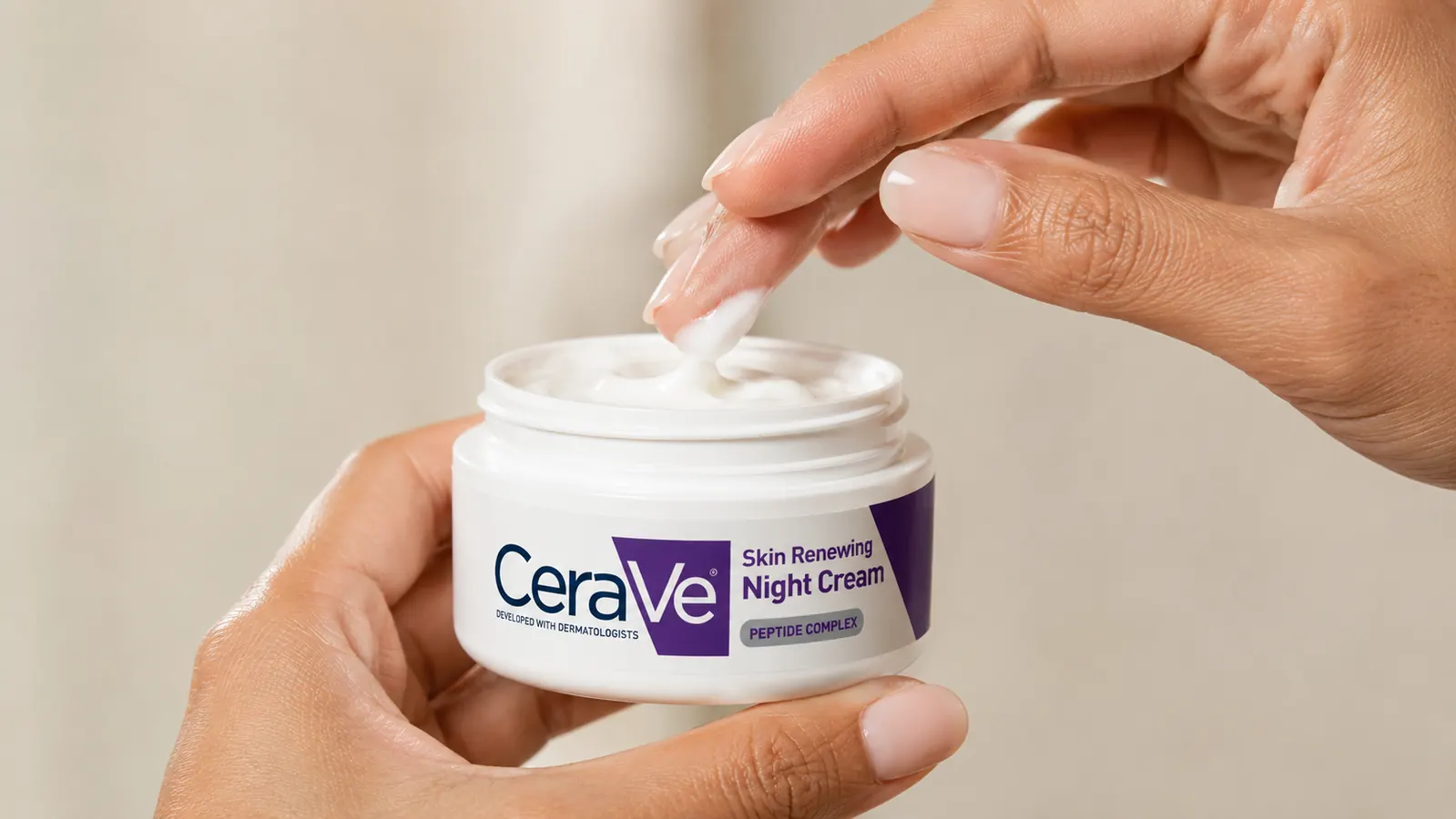 Close-up of fingers scooping a small amount of thick white night cream from a jar
