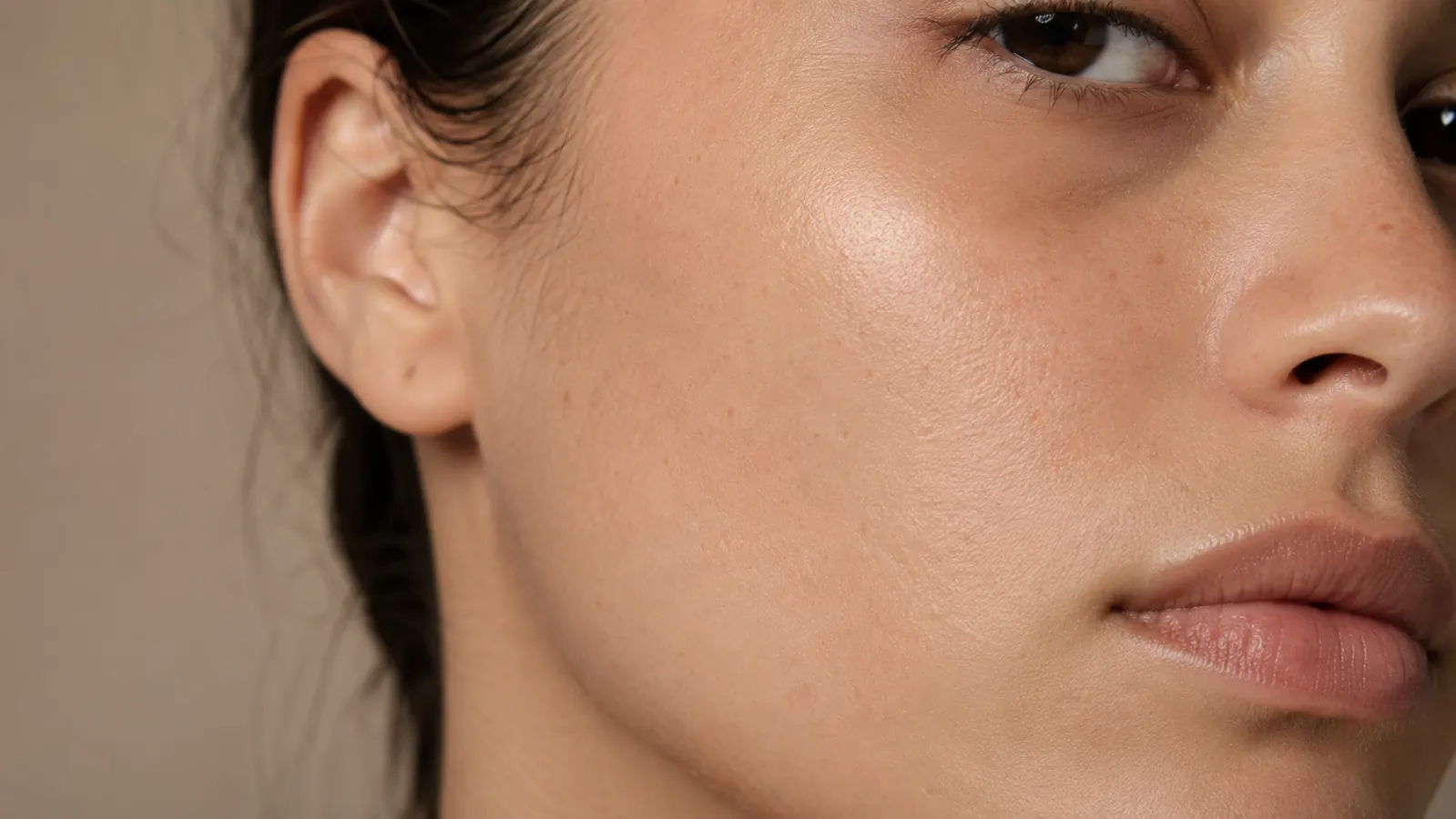 Close-up of smooth, calm skin on a jawline and cheek area, no visible redness or large pores, warm neutral background