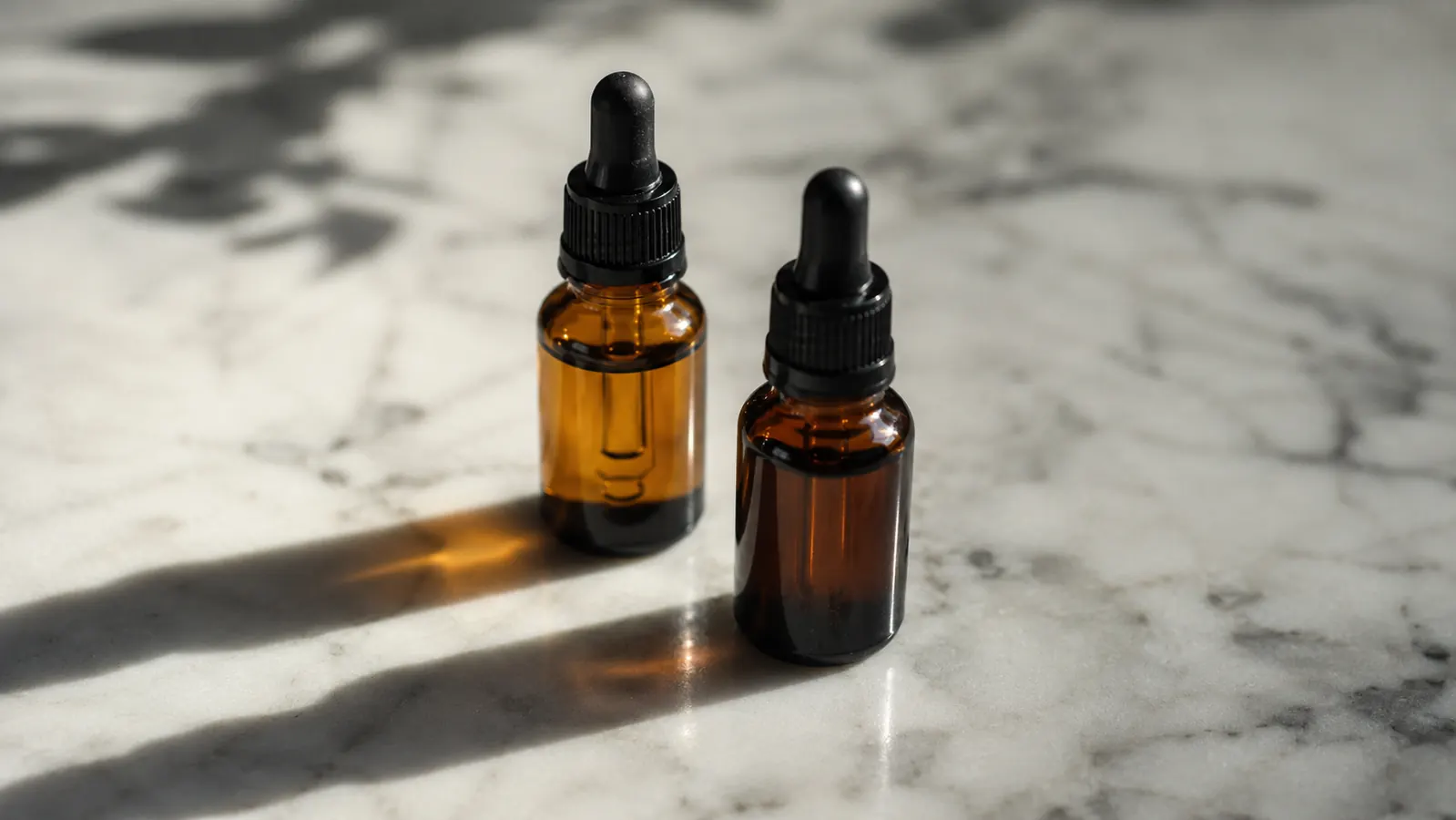 Two amber glass serum bottles on a white marble surface, one tipped with a faint orange tint showing oxidation